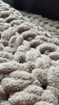 Vertical macro view pans slowly across the surface of a beige chunky-knit blanket. The soft plush texture of the chenille yarn and large loops are visible in detail.