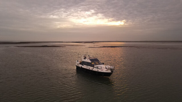 Aerial view of a motorboat floating on the calm waters of an estuary at sunset with mudflats visible in the background in Borough of Swale, England, United Kingdom.