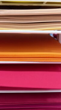 Different sheets of paper are arranged in stacks in a shop. The colors include pink, yellow, blue, and green, perfect for craft activities and school work.