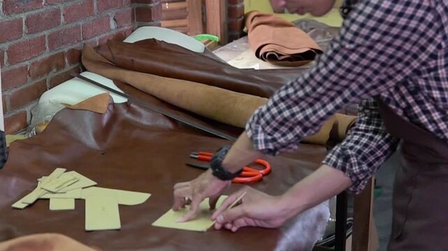 Middle-frame shot of a leather craftsman trimming yellow leather shapes at a busy workbench
