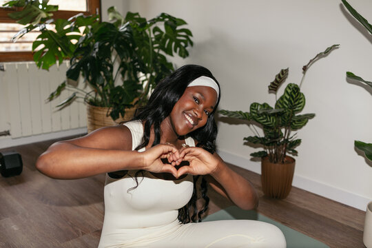 Black woman smiling making a heart shape with hands during home yoga workout
