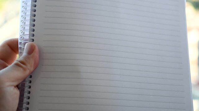 Hand holds open spiral notebook with blank lined pages ready to write on