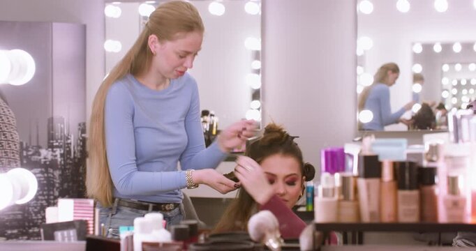 Salon styling. Woman beauty. Professional hairdresser making coiffure creating curls using curling irons in studio workplace.