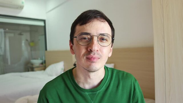 Happy man with glasses looking at the camera, puckering his lips, and blowing a romantic air kiss with his hand, showing affection and love in a friendly gesture from a personal point of view