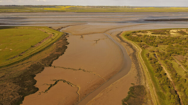 Aerial view of tidal mudflats and winding river channels in the Swale estuary, surrounded by green salt marshes and agricultural fields in the Borough of Swale, England, United Kingdom.