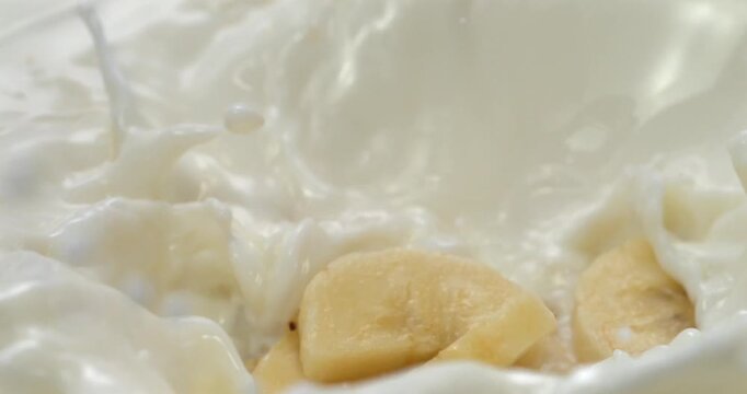 Banana slices falling into milk or yogurt with splash in super slow motion