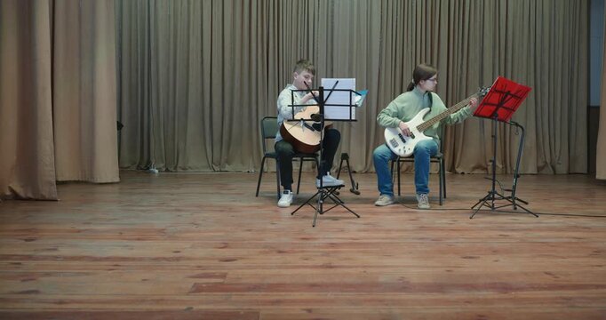 Boy and Girl Practice Playing Music on Stage. Kids Play Guitar and Bass Guitar. 4K 10-bit