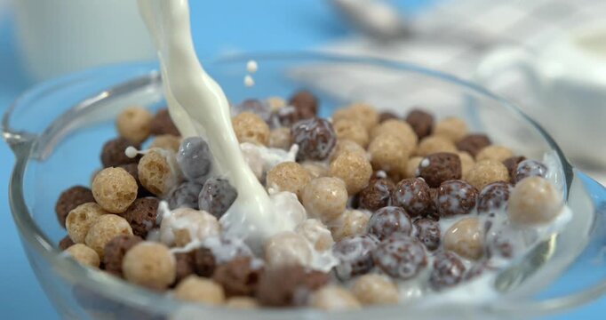 Milk pouring into wheat cereal corn balls in bowl with splash in super slow motion