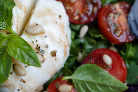 A plate shows fresh mozzarella cheese next to sliced tomatoes and green leaves. Basil and pine nuts are sprinkled on top. This dish is part of a summer meal enjoyed outdoors. top view