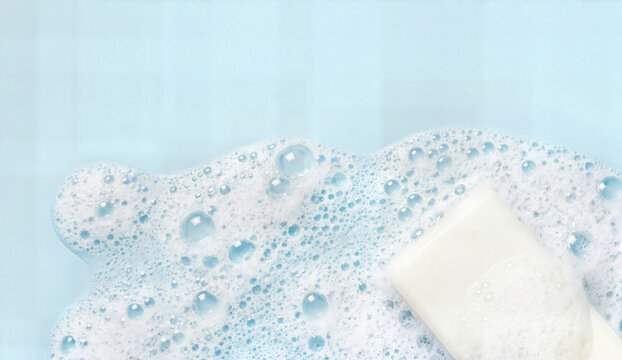 White soap bar in light blue bubbly foam, gentle cleaning, skincare product, hygiene concept, top view, minimal background.