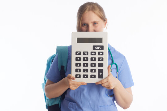 A nursing student in blue scrubs and backpack holds a large calculator, highlighting the financial and mathematical aspects of healthcare training and medical school.