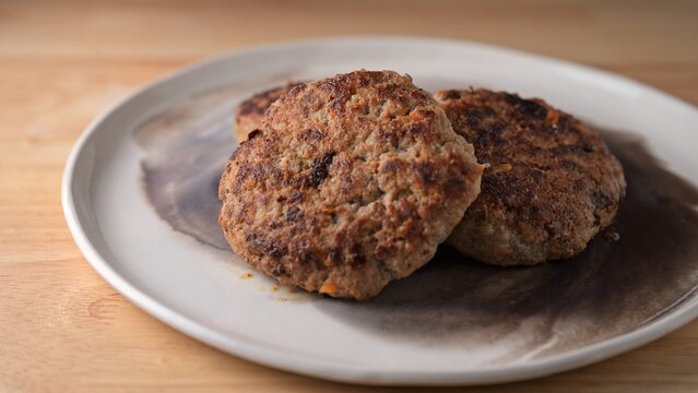 Beef and turkey patties with carrot on ceramic plate on wooden table. Food photography with selective focus. Homemade meat cutlet and cooking concept. Close-up shot.