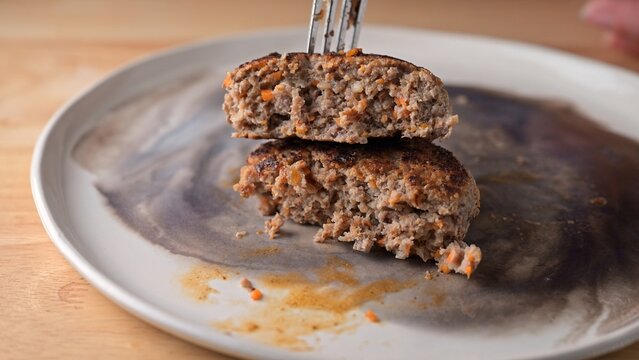 Cut juicy beef and turkey patties stacked on ceramic plate with fork. Food photography. Homemade meat cutlet and meal prep. Close-up shot.