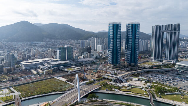 Aerial view of the modern skyline of Busan, featuring prominent skyscrapers, a cable-stayed bridge, and urban construction, set against rolling hills in Busan, Busan, South Korea.