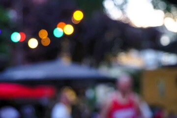 Fototapeta premium Abstraktes Motiv von Sommerfest mit bunten runden Lichtern vor hohem Baum und über blauem Zeltdach und Leuten am Abend im Sommer