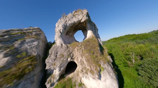 Cinematic FPV drone flight through a natural rock arch at Maczuga Herkulesa in southern Poland. Unique limestone formation surrounded by forest in the Jura region.
