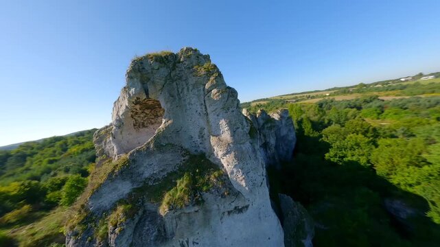 Cinematic FPV drone flight through a natural rock arch at Maczuga Herkulesa in southern Poland. Unique limestone formation surrounded by forest in the Jura region.