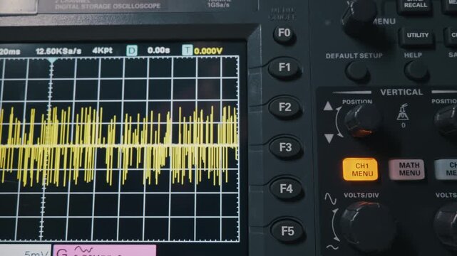A detailed close-up zooms out from a digital oscilloscope screen, revealing the yellow waveform of an electrical signal. Concept of electronic engineering, data analysis, and diagnostic technology.