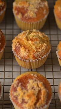 Orange muffins with almond flour crumb topping on cooling rack. Dessert food photography. Homemade bakery, pastry and snack concept. Vertical close-up shot.