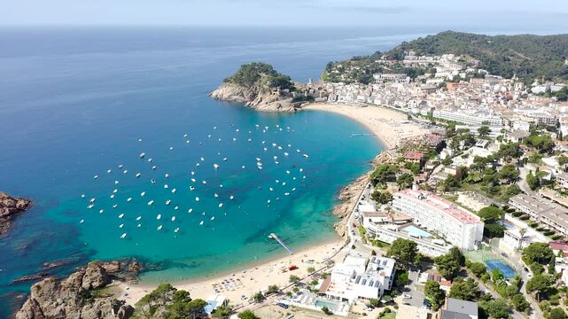Aerial view of Tossa de Mar, a historic Costa Brava town crowned by its medieval walls, overlooking a beautiful sandy beach and turquoise Mediterranean waters. 