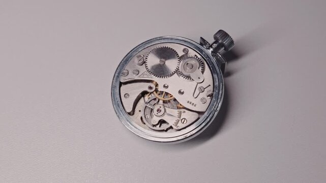Close-up view of a vintage mechanical stopwatch movement with moving gears and balance wheel on a white table. Concept of precision engineering, old technology, and the passing of time.