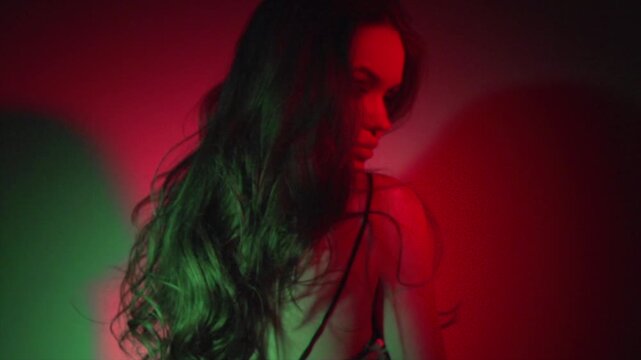 Sexy Beauty model girl with long hair dancing in colorful UV light, party, night club. Beautiful sensual brunette woman posing in darkness. Perfect make-up. Slow motion. 