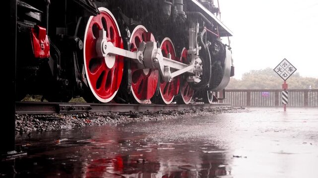 Vintage steam locomotive wheels on railway tracks in heavy rain