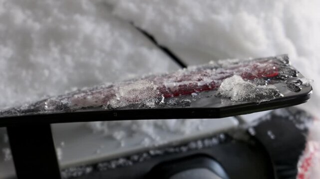 A close-up of a car's spoiler and taillight covered in a thick layer of melting ice and snow. This shot evokes the cold and harsh conditions of winter weather and driving.