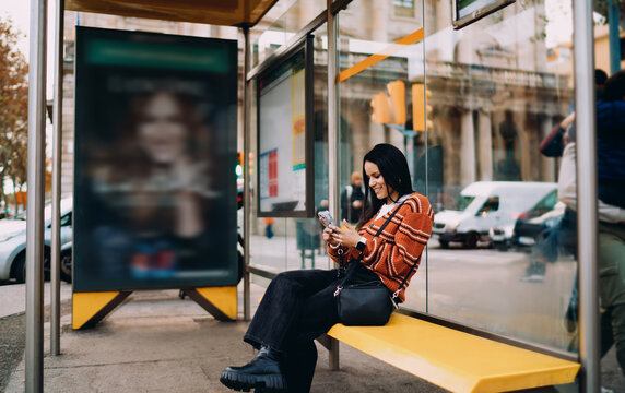 Cheerful Latin woman with radiant smile using smartphone, leaning on wall night street, authentic lifestyle photography, mobile communication, digital nomad, startup culture, inclusive beauty.