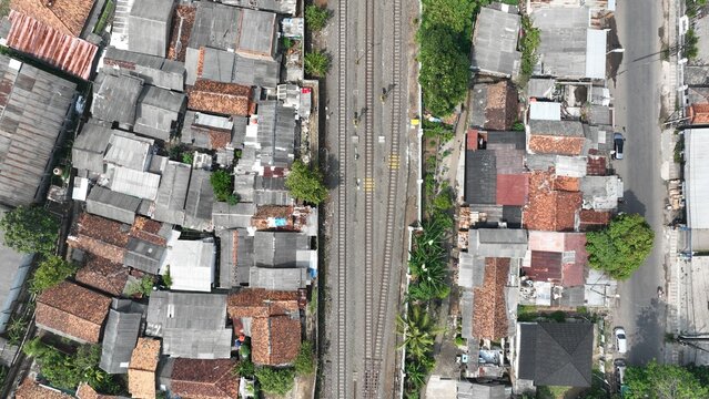 Aerial view of railway tracks running through a dense residential neighborhood with terracotta rooftops and lush trees in Kecamatan Serang, Banten, Indonesia.