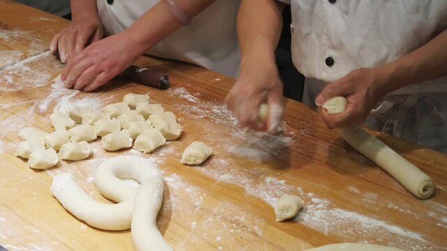workers prepare dough on floured board in food industry. skilled workers shape dough using manual techniques. fresh dough is rolled and cut into portions for chinese cuisine