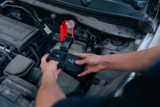 Male hands connect portable power bank jump starter to car battery. Emergency roadside assistance, automotive service, modern vehicle maintenance or problem solving concept.