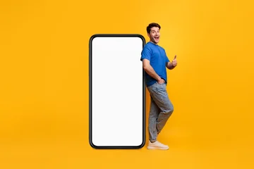 Fototapeten Pony Happy Male Appearing Excited While Standing Beside A Large Smartphone With An Empty Screen, In A Bright Studio Setting. Promoting New App Or Digital Service, Advertising Concept.  © Prostock-studio
