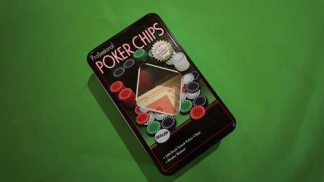 A close-up shot of a poker chip set box, featuring colorful poker chips and playing cards, lying flat on a vibrant green screen background. The video maintains a steady, top-down perspective