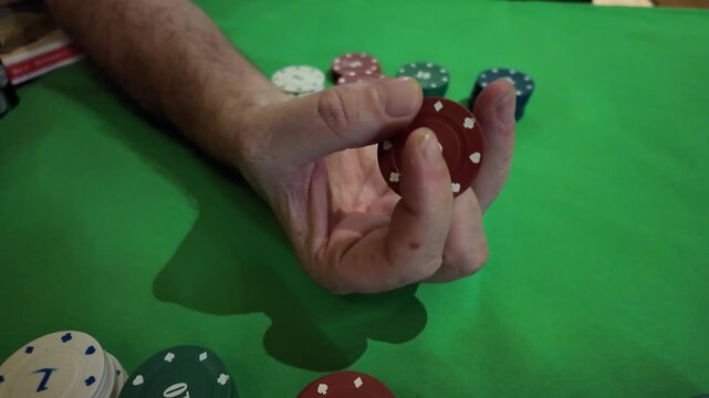 A close-up shot focuses on a person's hand as they expertly manipulate a single red poker chip. The hand moves the chip with skill, showcasing a common action seen in card games like poker. The