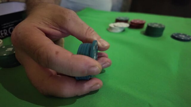 A close-up view of a person's hand stacking blue poker chips, each marked with '25', on a vibrant green felt table. The mood is focused and strategic, evoking the atmosphere of a casino or game night