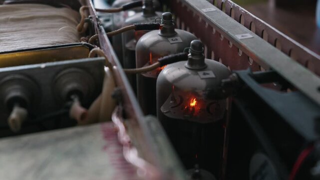 Glass vacuum tubes operate inside a homemade electronic audio amplifier. Internal filaments glow bright orange. The metal chassis contains visible wiring and a large power transformer.