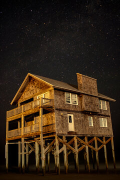 A beach house under a starry night sky is standing alone against the waves along the Outer Banks.