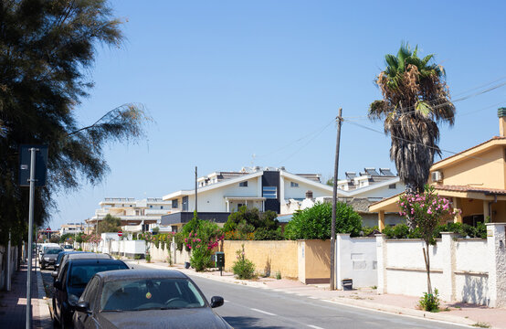 Focene, Rome, Italy &ndash; July 18, 2024: Residential street in Focene near Rome, Italy, featuring modern houses, parked cars, palm trees and Mediterranean vegetation under a clear summer sky.
