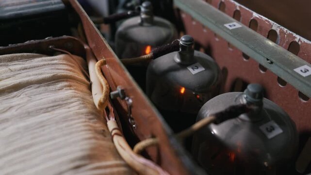 Vacuum tubes glow with a warm orange light inside a custom homemade amplifier chassis in low light. Concept of analog audio fidelity, vintage radio engineering and retro electronics hardware