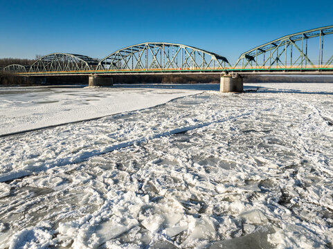 Old metal bridge with traffic over river with ice floes.
