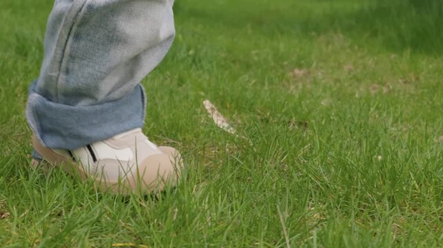 A young child wearing cuffed jeans and sneakers takes steps on a lush green lawn next to an adult. Concept of early childhood development, growth, and parental support in nature.