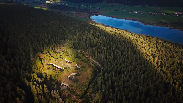 Aerial view of Fort Guyot in a dense forest, with sunlight highlighting historic stone fortifications near a blue lake in Les Rousses, Bourgogne-Franche-Comte, France.