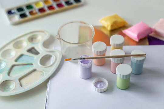 Creative painting materials with pastel acrylic paints, clean brush, watercolor set, transparent beaker, blank sheet creating organized artist workspace for crafts, illustration, creative learning