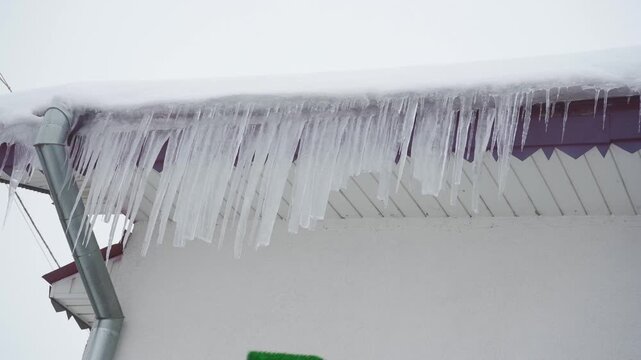 Man knocks sharp icicles off roof eaves, Cleaning the roof of a house from large dangerous icicles and snow with a brush or mop in winter