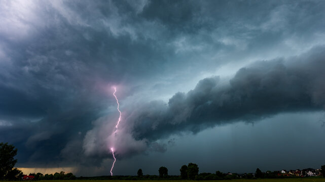 Dramatic lightning bolt striking from a powerful shelf cloud during severe summer thunderstorm. Extreme weather landscape