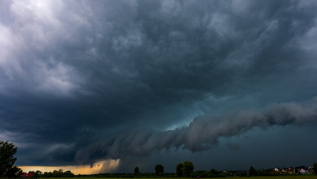 Massive shelf cloud incoming over green fields. Severe supercell thunderstorm front approaching in rural area