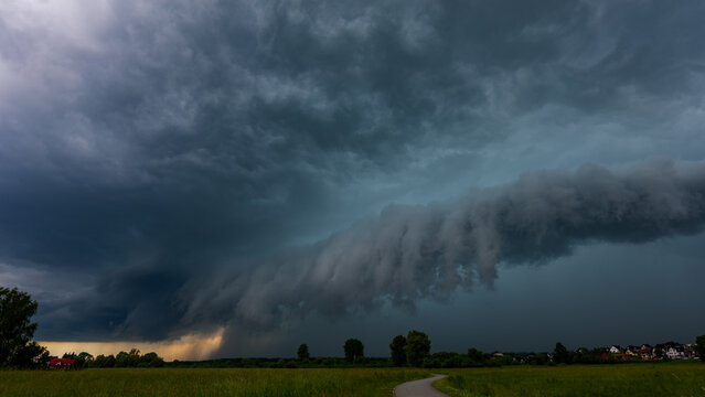 Massive shelf cloud incoming over green fields. Severe supercell thunderstorm front approaching in rural area