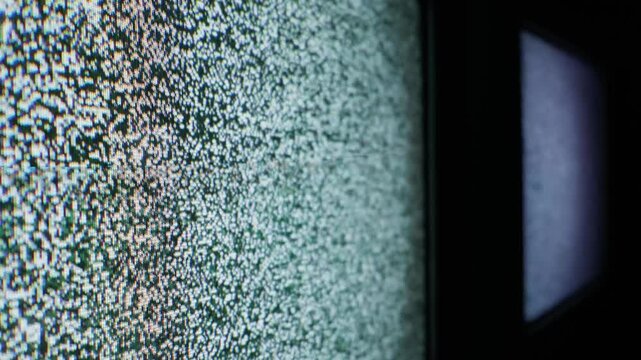 A classic television monitor displays flickering white noise and analog static. The screen features sharp focus on individual pixels and distinct CRT scan lines, conveying a sense of signal