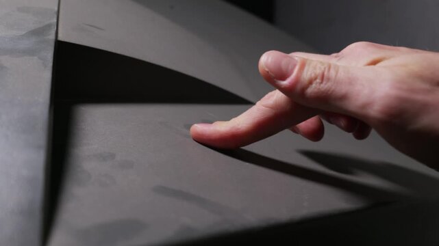 Male index finger swipes across a heavily dusty dark matte surface. A clean trail appears behind the finger. Side lighting emphasizes the thick layer of dirt and contrast.